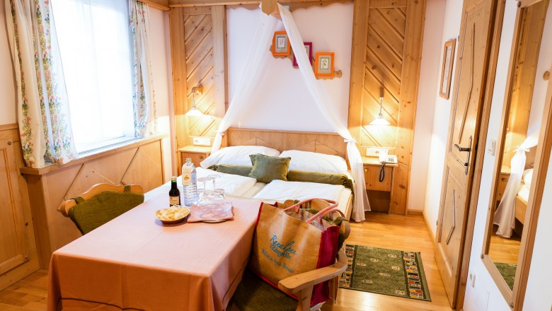 Double room Cat. A, © Scharfegger´s Raxalpen Resort Cozy double room with wooden furniture, a table with drinks and snacks, and a bed with canopy.