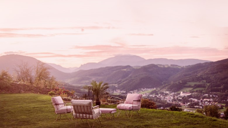 View from the Fernblick, © Matthias Kronfuss Seating area on a meadow with mountain views at sunset.