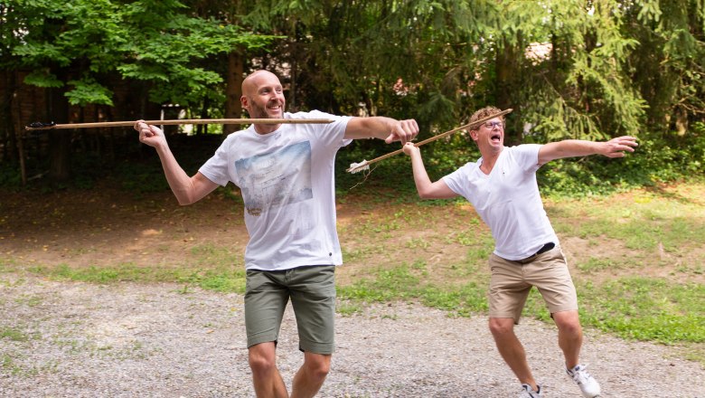 MAMUZ, active management, © Roman Jandl Two men throw spears outdoors, surrounded by trees.