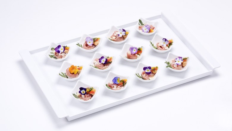 Trabitsch Catering, © Trabitsch Catering A tray with twelve small bowls decorated with ham, edible flowers and herbs.