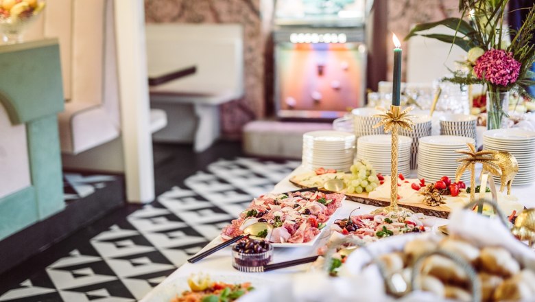 Buffet, © Matthias Kronfuss A rich buffet with various dishes, piles of crockery and decorative candlesticks in a stylish room.
