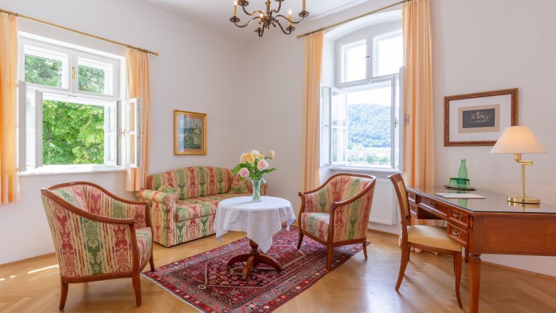 Hotel suite at the Hotel Richard Läwenherz, © Chris Saupper Elegant living room with antique furniture, two windows, a table with flowers, a desk and a carpet on a wooden floor.