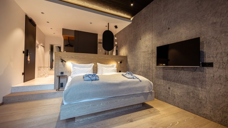 Refugium Lunz, © Niederösterreich Werbung / Maximilian Pawlikowsky Modern bedroom with wooden floor, gray wall, double bed and flat screen TV.