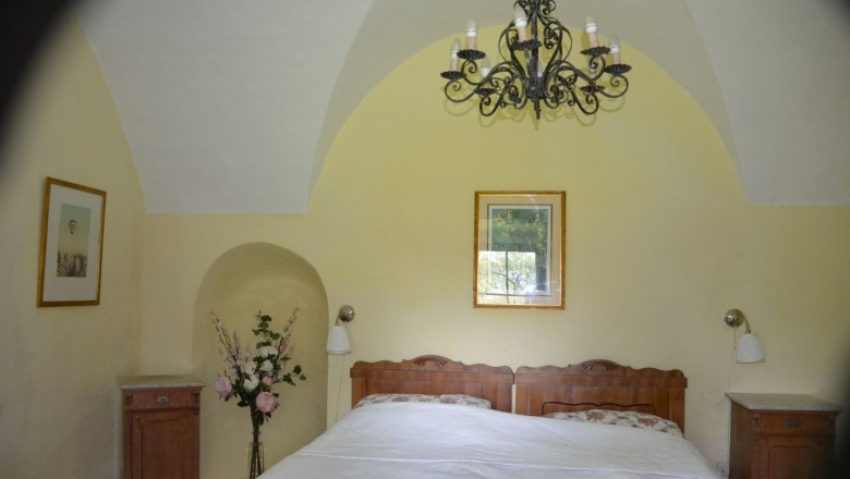 Vacation apartment Rossarium bedroom 1, © Renaissanceschloss Greillenstein Bedroom with double bed, yellow walls, a chandelier and flowers in a vase.