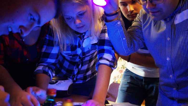 TEAMbuilder, Escape Room, © TEAMbuilder Group of people solves puzzles in an escape room with UV light.