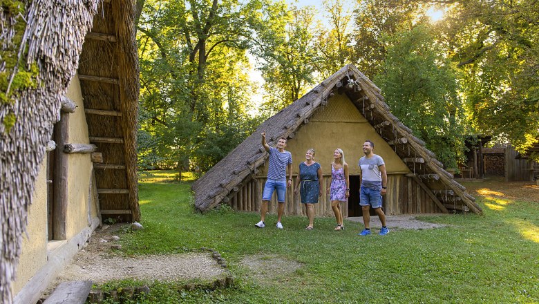 MAMUZ Schloss Asparn, © Roman Jandl Four people stand outside a historic building with a thatched roof.