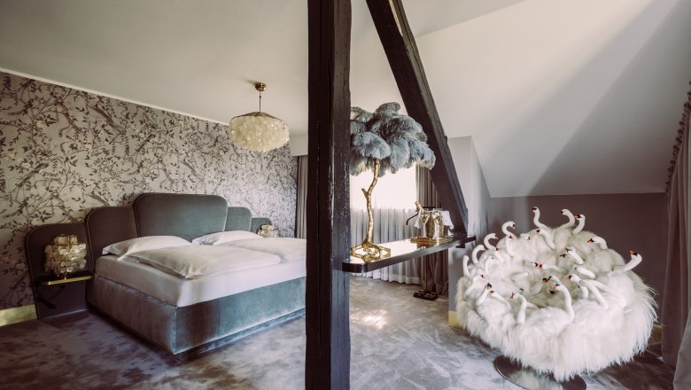 Bridal suite, © Matthias Kronfuss Luxurious bedroom with large bed, decorative wallpaper, chandelier and extravagant armchair with swan design.
