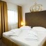 Double room bed, © Hotel Kaiser Franz Josef A double room with a large bed, golden curtains and two bedside tables with lamps.
