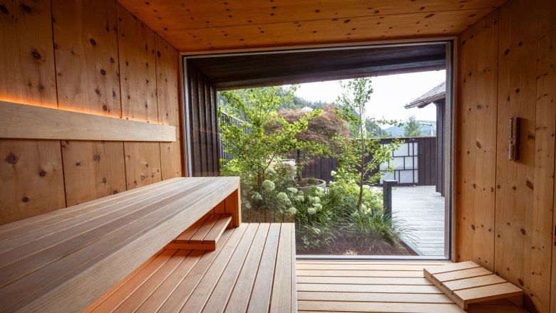 Refugium Lunz, © Niederösterreich Werbung / Maximilian Pawlikowsky Interior view of a modern sauna with wooden walls and benches, view of a garden through a large window.