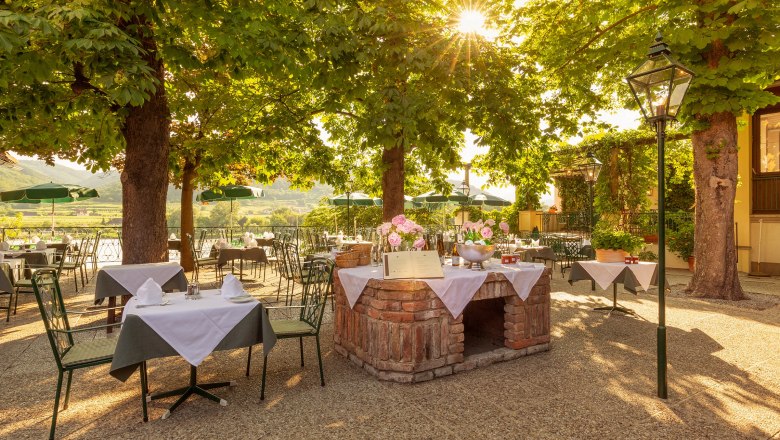 Restaurant terrace at the Hotel Richard Löwenherz, © Chris Saupper A sunny outdoor area of a restaurant with covered tables under trees.