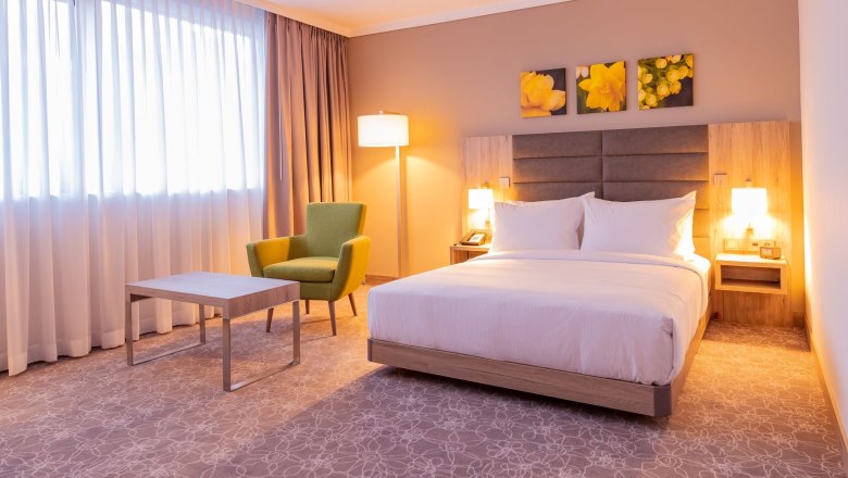 Room, © Hilton Garden Inn Wiener Neustadt Modern hotel room with double bed, green armchair, table and floor lamp.