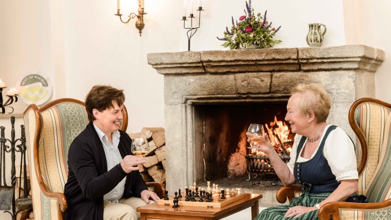 Fireplace room Hotel Richard Löwenherz, © BOW Rita Newman Two women are sitting in armchairs in front of a fireplace, drinking wine and playing chess.