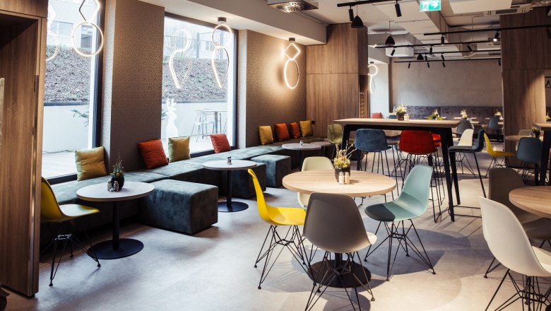 Hotel Rainers21, © Hotel Rainers, Anna Rauchenberger Modern hotel restaurant with colorful chairs and tables, large windows and stylish lighting.