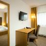 Double room, © Hotel Kaiser Franz Josef A hotel room with a double bed, a desk and chair, a TV on the wall and yellow curtains.