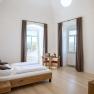 Room example in the guest house at Göttweig Abbey, © Robert Herbst Bright double room with wooden bed, table and chairs, two windows with curtains and a cross on the wall.