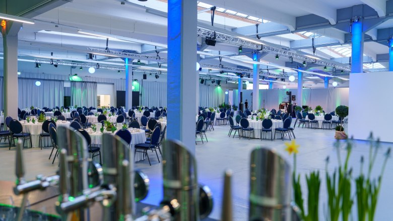 Glanzstoff Events, Konerei, © Bollwein Large function room with round, laid tables and blue lighting.