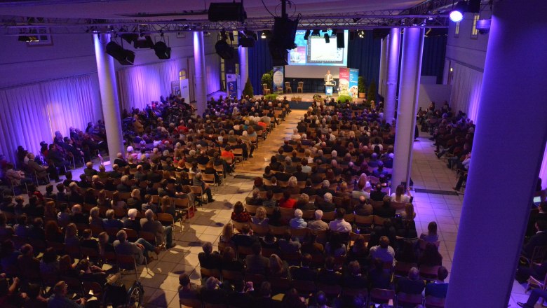 Atrium Tulln, © Stadtgemeinde Tulln A fully occupied event room with stage and audience, illuminated in blue light.