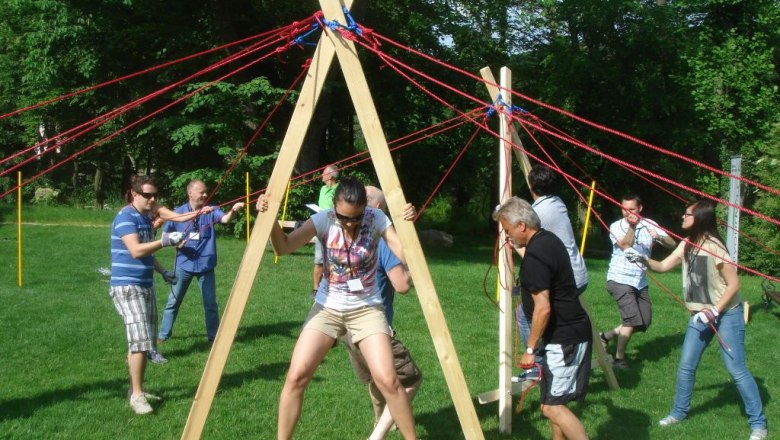 TEAMbuilder, © TEAMbuilder People at an outdoor team-building event with a wooden structure and ropes.