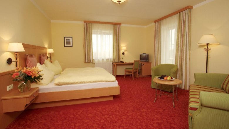 A cozy hotel room with a double bed, sofa, table and TV. Yellow walls and red carpets dominate the room.