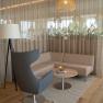 Modern seating area with gray armchair, patterned sofa, round wooden table and floor lamp in front of a curtain.