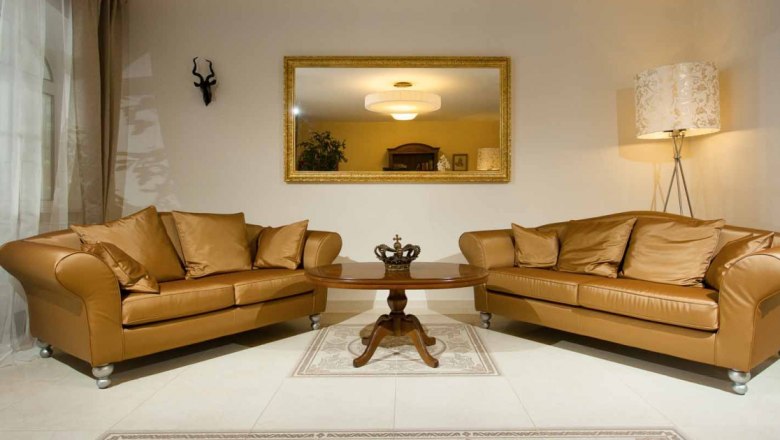 Elegant lobby with two brown sofas, a round wooden table and a large mirror on the wall.