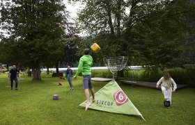 People play an outdoor throwing game with large dice on a meadow.