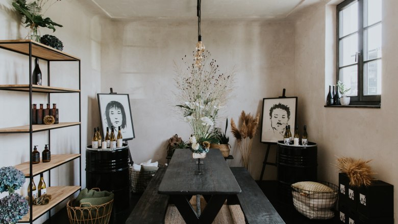 A stylishly furnished room with a wooden table, shelves, plants and works of art on the walls.