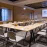 A modern seminar room with a U-shaped table arrangement, chairs, notepads and glasses. A screen with the Hilton Garden Inn logo on the wall.