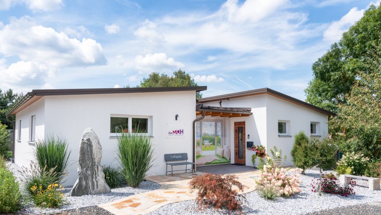 Modern, white building with garden and gravel path, blue sky in the background.