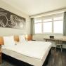 Modern double room with large bed, artwork on the wall, desk and flower arrangement.