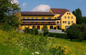 Yellow hotel building with flower balconies, surrounded by green landscape.