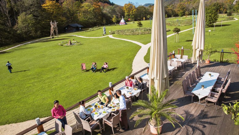 Terrace of the seminar and event hotel Krainerh&uuml;tte with guests eating, surrounded by green meadows and forest.