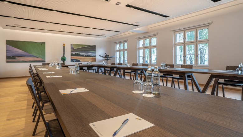 Seminar room in the Hotel Spitzerberg with long wooden tables, chairs, water bottles and writing materials.