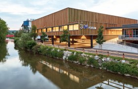 Modern Messe Wieselburg building with wooden fa&ccedil;ade and river in the foreground.