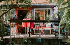 Colorful terrace in front of the location with red chairs and table, surrounded by plants and decorations.