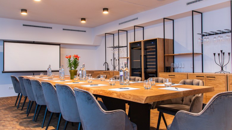Modern conference room with large wooden table, gray chairs and presentation screen.