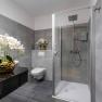 Modern bathroom with gray tiles, shower, toilet and orchids in golden vases.