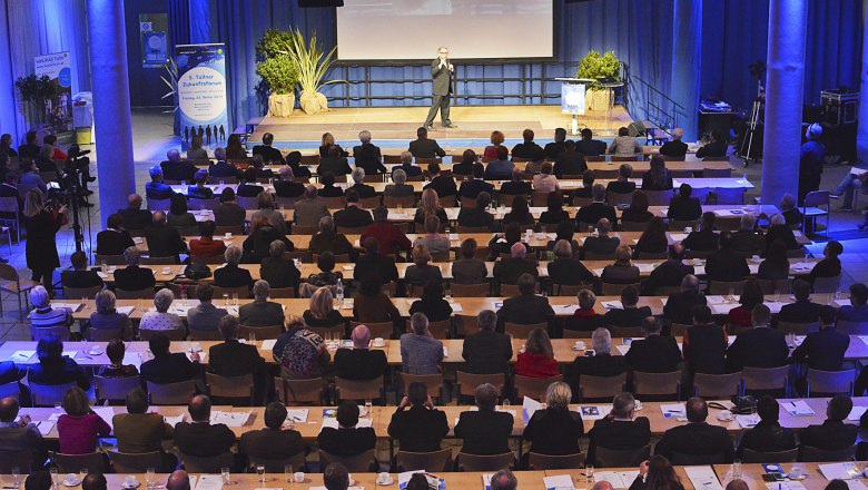 A speaker addresses a large audience in a conference hall.