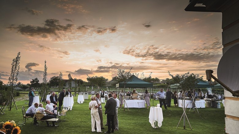 Garden party with guests at sunset, tables and tents on a meadow.