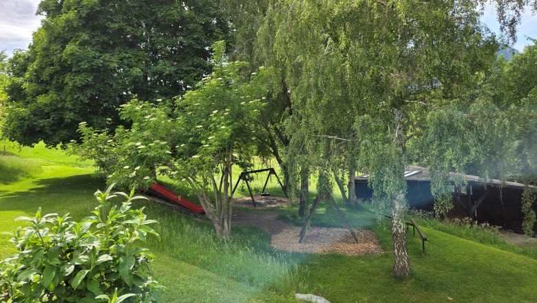 A green garden with trees, a swing, and a slide.