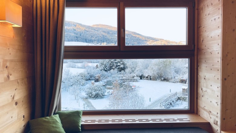 View from a wooden window of a snowy landscape with mountains in the background.