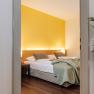 Hotel room with yellow wall, double bed and plant in the foreground.