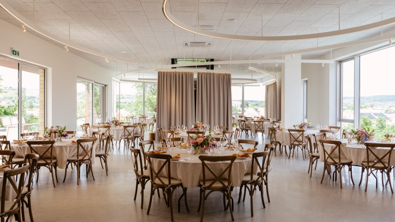 Elegant function room with round tables, chairs and floral decorations.