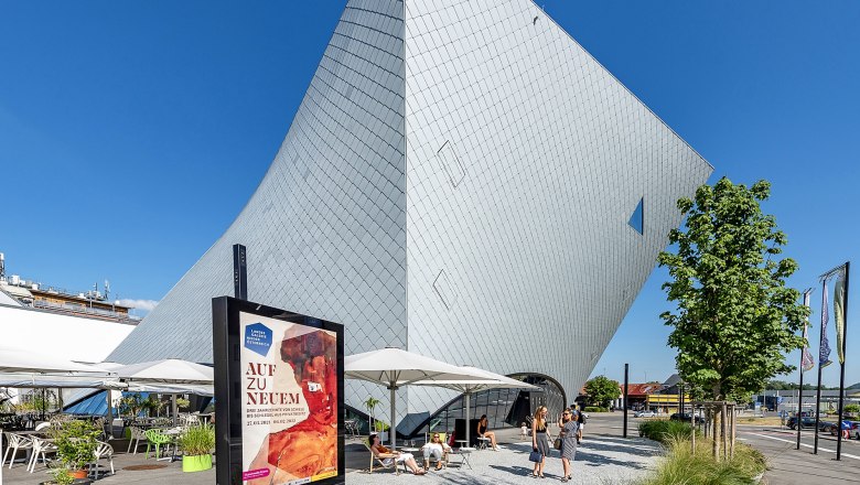 Modern architecture of the Landesgalerie Niederösterreich in Krems with visitors and advertising poster in the foreground.