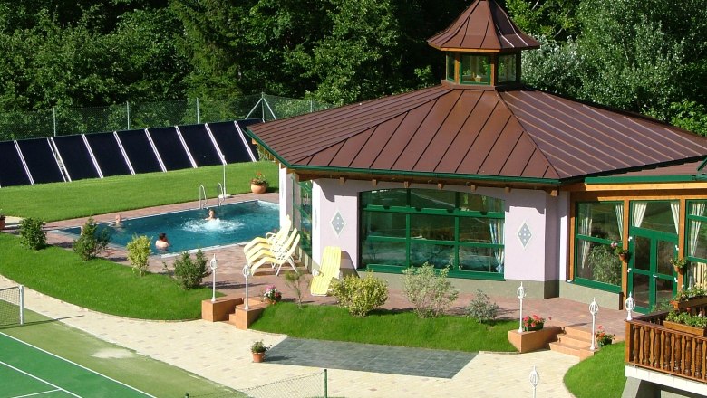 Exterior view of a wellness area with pool and pavilion surrounded by greenery.