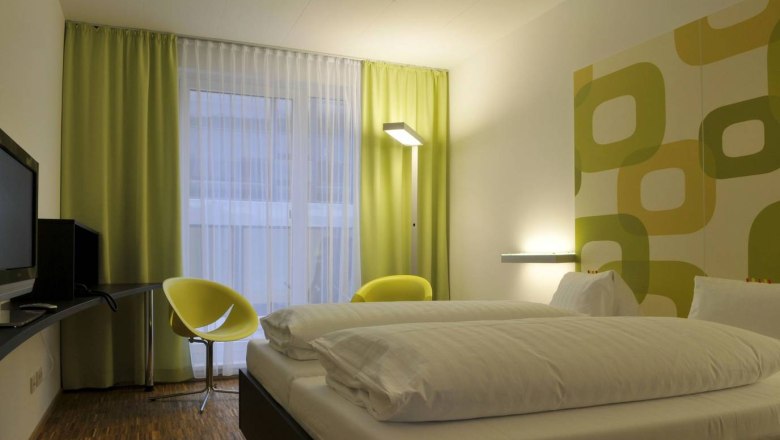 Modern hotel room with double bed, green-yellow curtains and wall decor.