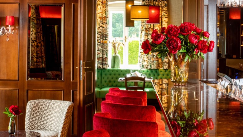 Elegant restaurant with red velvet chairs, chandelier and floral decorations.