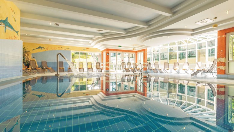 A bright indoor pool with sun loungers and a jet of water in the pool.