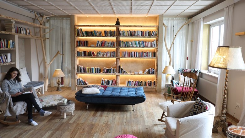 Cozy library with a large, illuminated bookshelf, armchairs and a person reading.