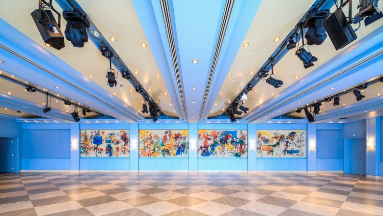 Interior view of the Badener Saal in the Congress Center Baden with blue ceiling, colorful murals and diagonal floor tiles.